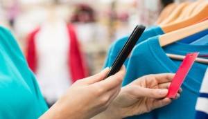 Woman scanning price tag of casual apparels through smart phone at clothes shop. Horizontal shot.